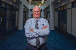 Man wearing a light blue shirt and a tie smiles for a portrait