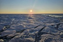 A frozen body of water with the sun low on the horizon